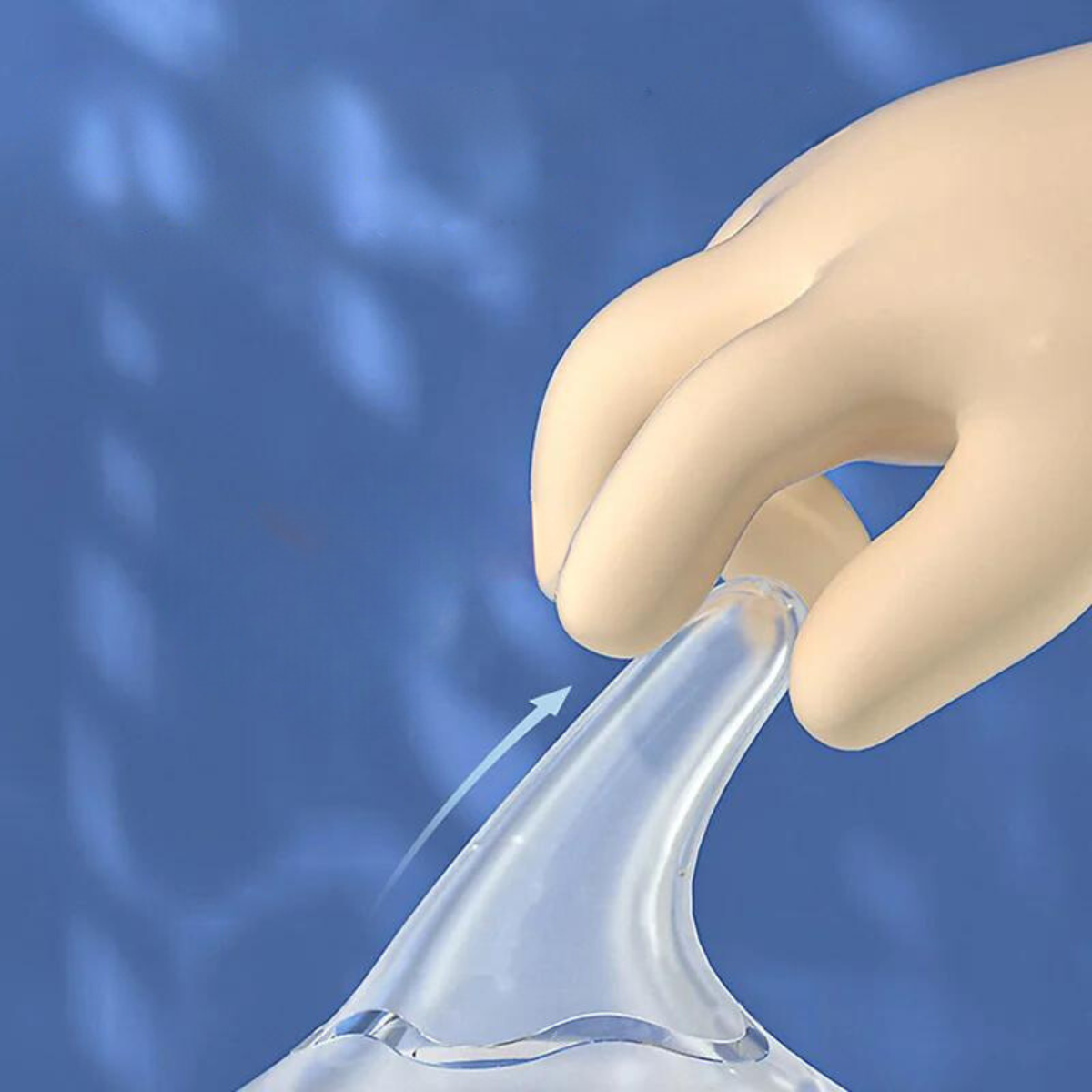 Close-up of a hand gently pinching the soft silicone nipple of a baby feeding bottle, demonstrating its flexibility against a blue background.