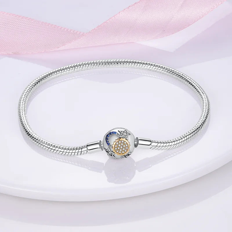 A silver bracelet with a circular charm featuring a celestial design with a moon, stars, and sun motif in gold and blue accents.